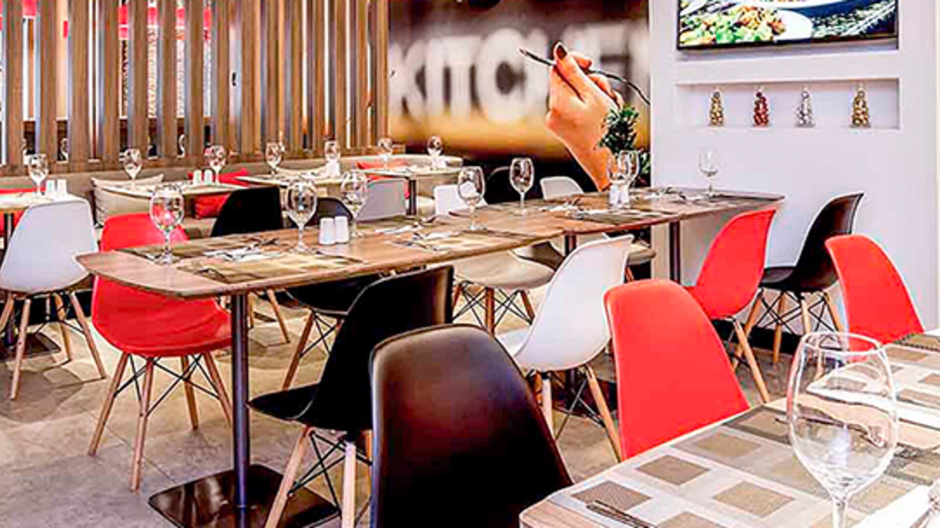 Restaurant with wooden tables, red and white chairs, place settings and decorative wall panels at Ibis Lima Reducto Miraflores.