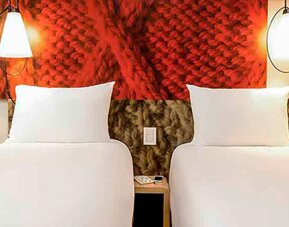 Twin beds with white linens, red textured headboard panels, bedside tables and wall-mounted lamps at Ibis Lima Reducto Miraflores.
