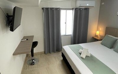 Guest room with double bed, pale green runner and cushions, wall-mounted television, desk and grey curtains at 12 Nights Hotel.