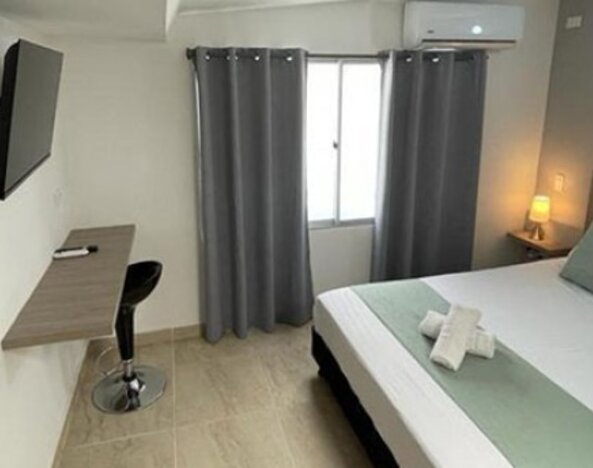 Guest room with double bed, pale green runner and cushions, wall-mounted television, desk and grey curtains at 12 Nights Hotel.