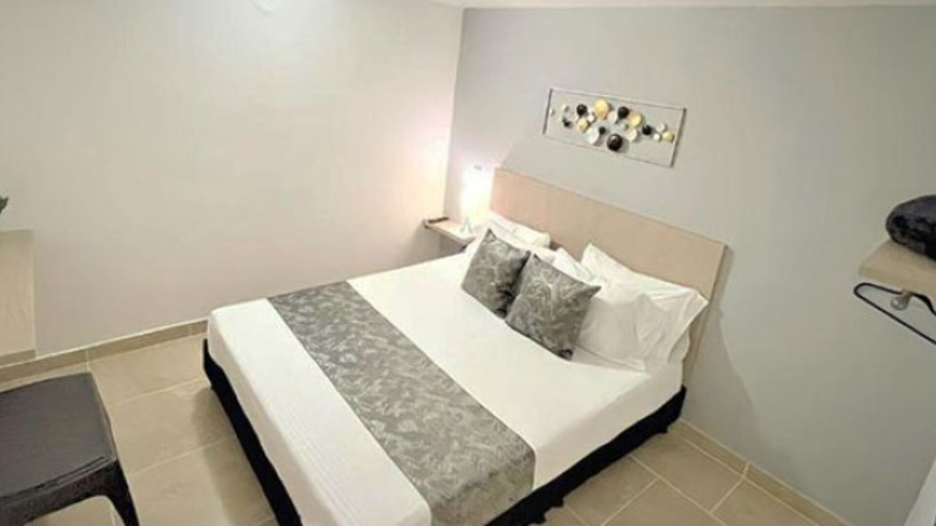 Guest room with double bed, grey patterned runner, matching cushions, bedside table and wall-mounted television at 12 Nights Hotel.