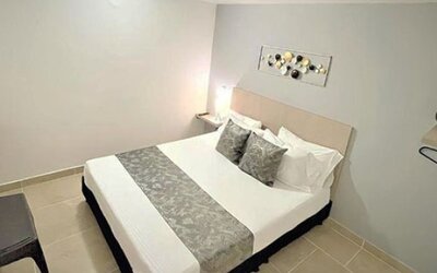 Guest room with double bed, grey patterned runner, matching cushions, bedside table and wall-mounted television at 12 Nights Hotel.