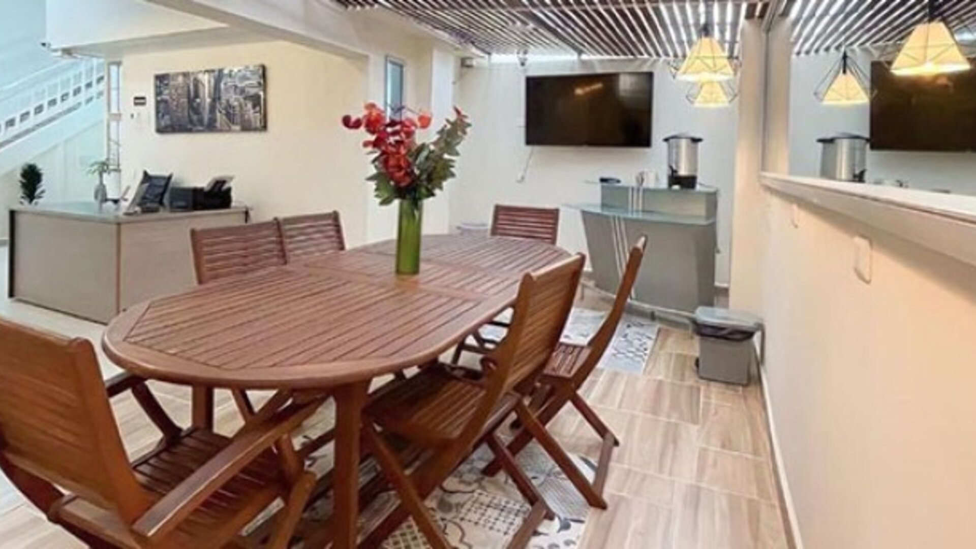 Dining area with wooden table and chairs, flower arrangement, pendant lights and staircase at 12 Nights Hotel.