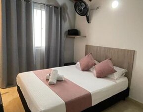 Guest room with double bed, pink accent cushions and runner, grey curtains, wall fan and wooden desk at 12 Nights Hotel.