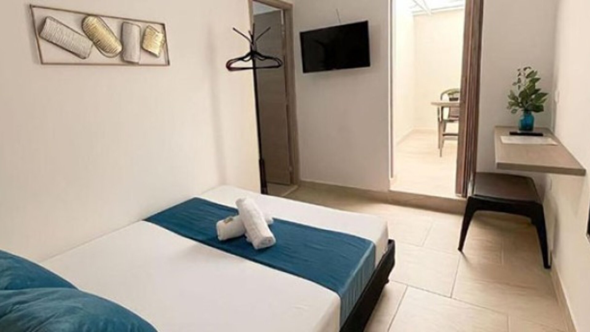 Guest room with bed, teal runner and cushions, wall-mounted television, dressing table and full-length mirror at 12 Nights Hotel.