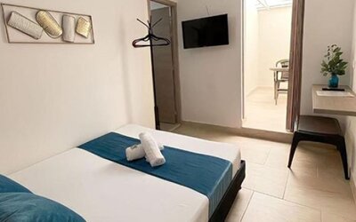 Guest room with bed, teal runner and cushions, wall-mounted television, dressing table and full-length mirror at 12 Nights Hotel.