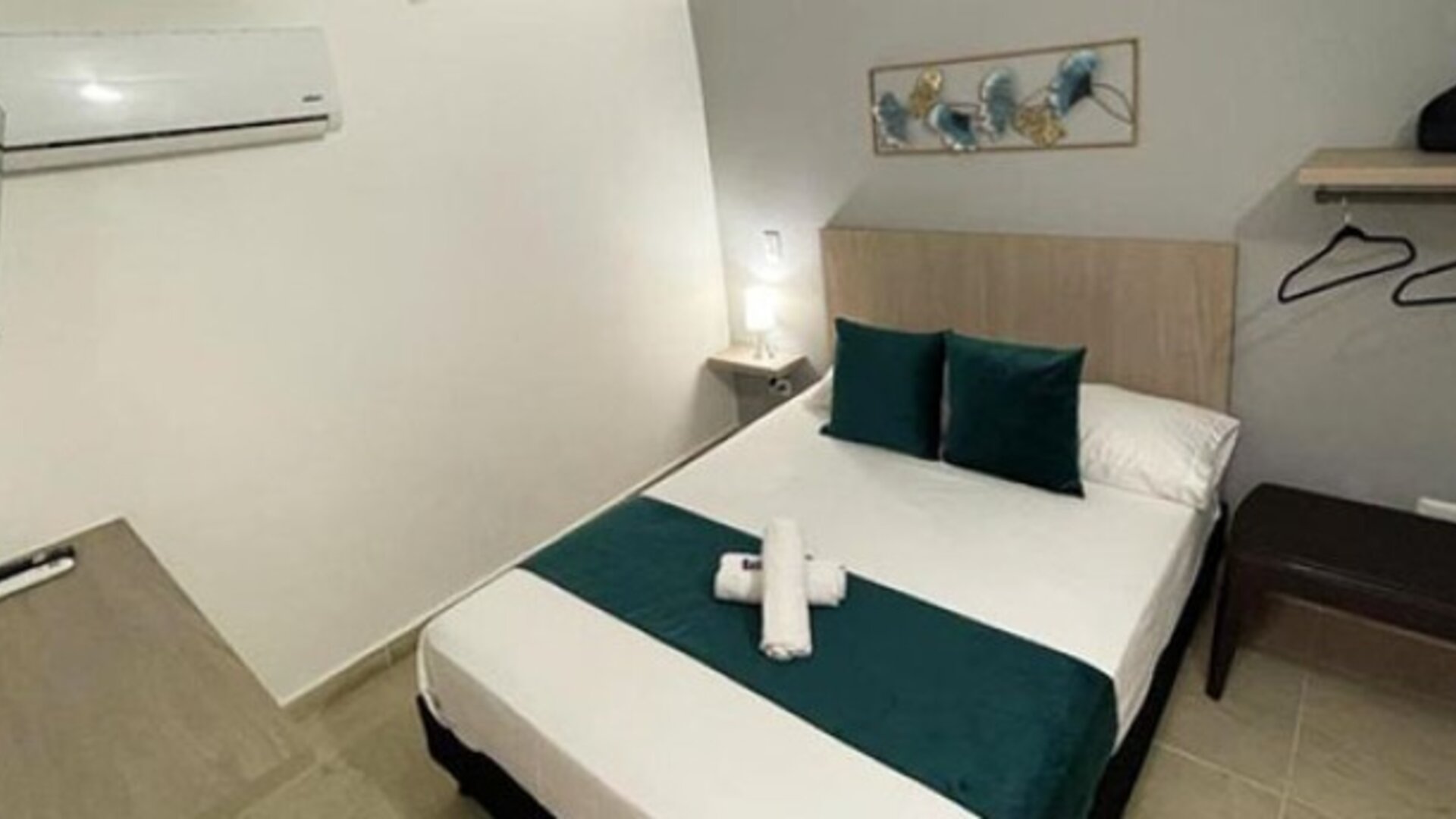 Guest room with double bed, teal bedding accents, wall-mounted television, air conditioner and open clothes rail at 12 Nights Hotel.