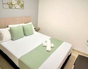 Guest room with double bed, green accent cushions, matching bed runner, wall-mounted television and wooden desk at 12 Nights Hotel.