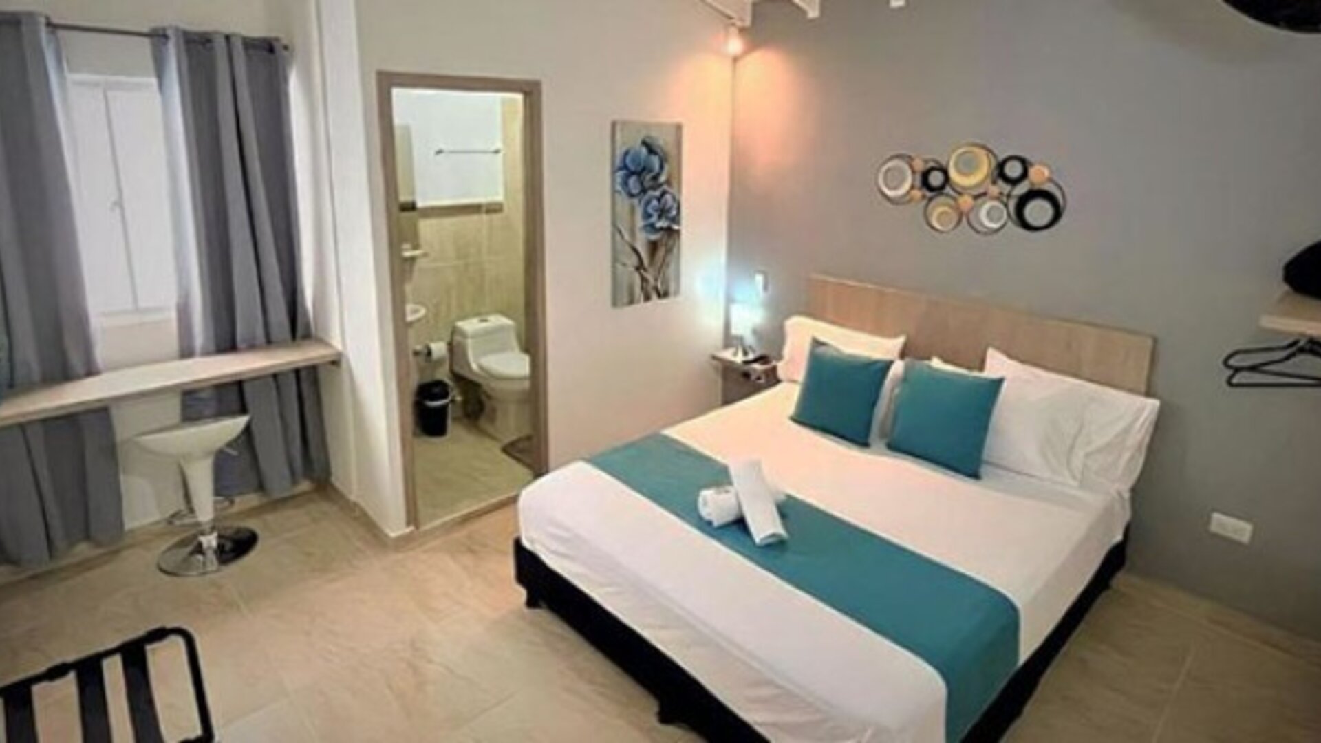 Guest room with double bed, teal runner and cushions, bedside lighting, desk and ensuite bathroom at 12 Nights Hotel.
