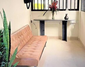 Sitting area with pink upholstered sofa, decorative cushions, tall potted plants and a small console table at 12 Nights Hotel.
