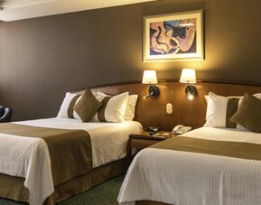 Twin guest room with two beds, white bedding, olive-green runners, framed artwork and bedside lamps at Hotel Misión Toreo Centro De Convenciones.