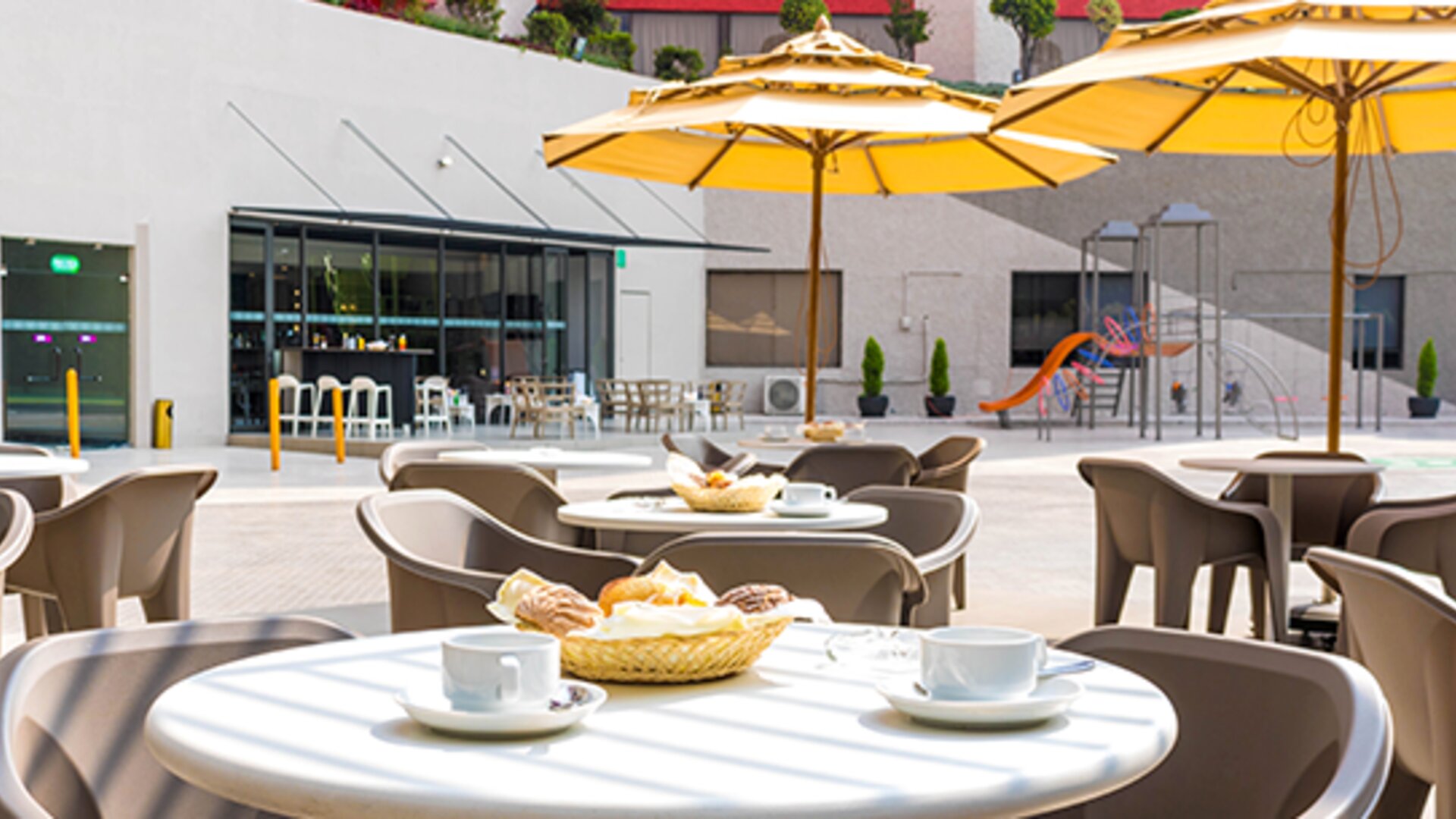 Outdoor dining terrace with round tables, chairs, yellow umbrellas and views of the courtyard at Hotel Misión Toreo Centro De Convenciones.