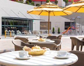 Outdoor dining terrace with round tables, chairs, yellow umbrellas and views of the courtyard at Hotel Misión Toreo Centro De Convenciones.