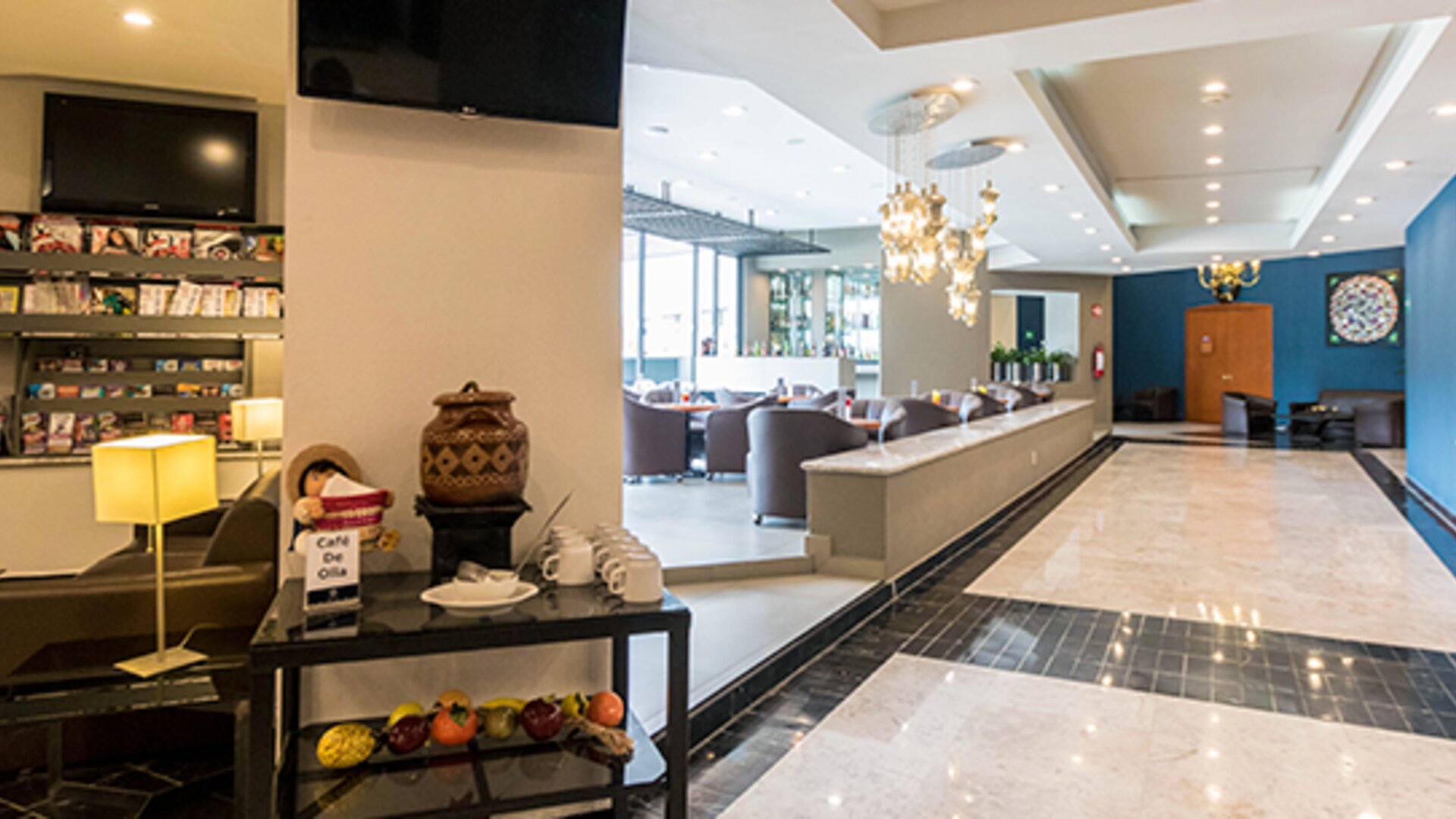 Hotel lobby with reception counter, lounge seating, decorative chandeliers and blue accent wall at Hotel Misión Toreo Centro De Convenciones.