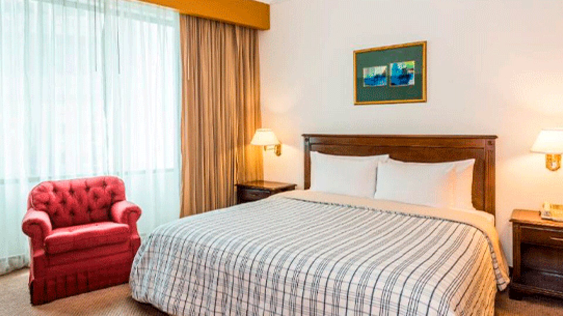 Guest room with double bed, striped bedding, red armchair, bedside lamps and a large curtained window at Hospedium Princess Hotel Panamá.