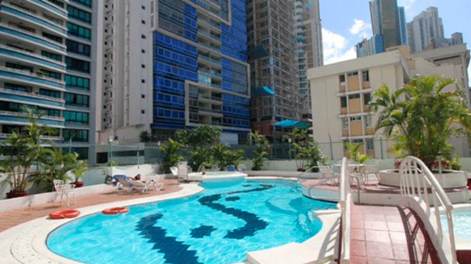 Outdoor swimming pool with turquoise water, sun loungers, palm trees and surrounding high-rise buildings at Hospedium Princess Hotel Panamá.