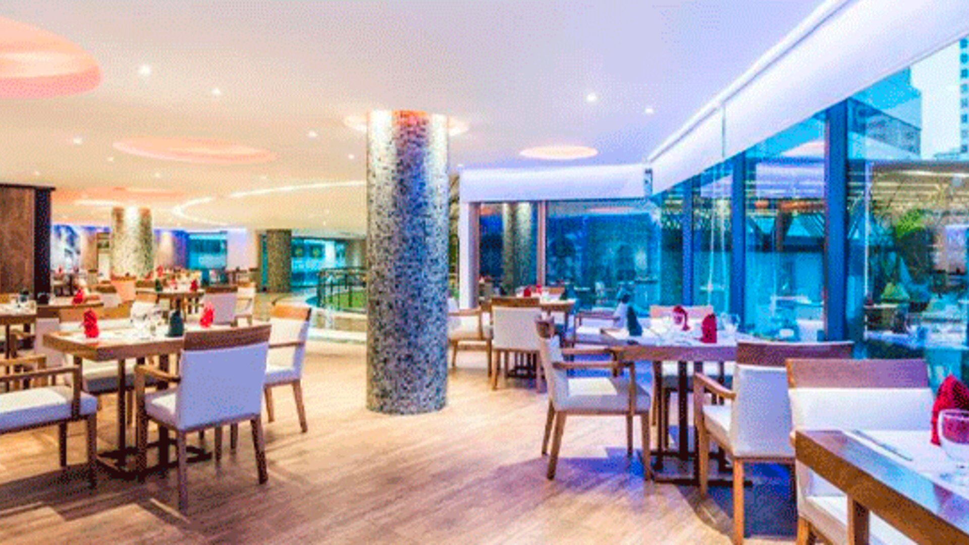 Hotel restaurant with neatly arranged tables, upholstered chairs, pendant lights and floor-to-ceiling windows at Hospedium Princess Hotel Panamá.