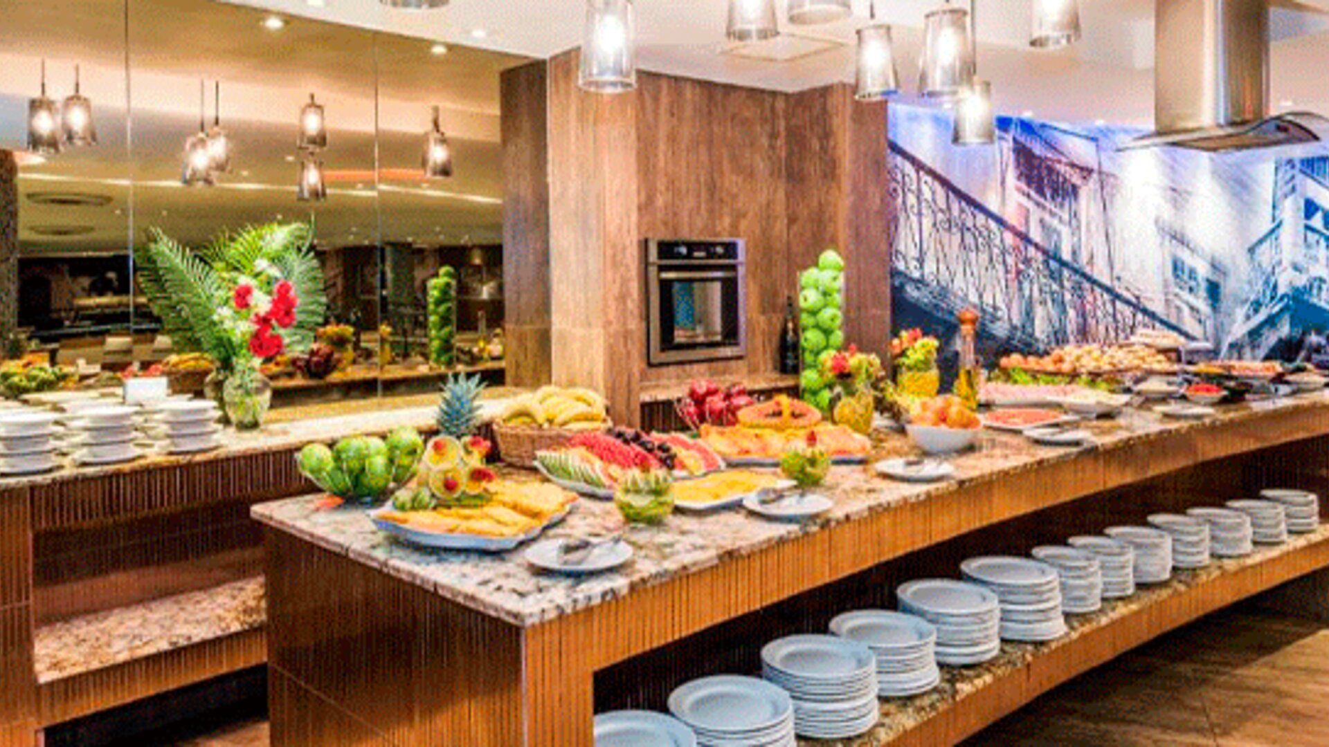 Breakfast buffet with fresh fruit, pastries, stacked plates and serving counters under pendant lighting at Hospedium Princess Hotel Panamá.