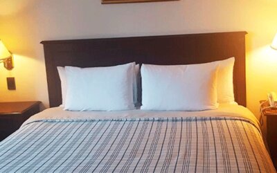 Guest room with double bed, striped bedding, dark wooden headboard and matching bedside tables with lamps at Hospedium Princess Hotel Panamá.