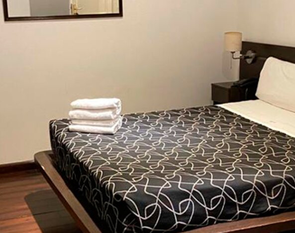 Guest room with double bed, black patterned bedding, folded white towels, bedside table and wall mirror at Bagu Buenos Aires.