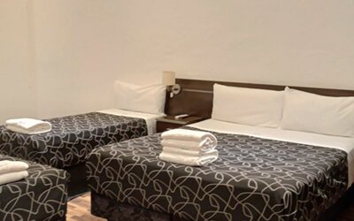 Guest room with one double bed and two single beds, patterned black bedding, white towels and dark bedside furniture at Bagu Buenos Aires.