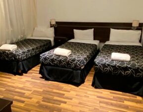 Guest room with three single beds, black patterned bedding, white towels, bedside lights and wooden flooring at Bagu Buenos Aires.