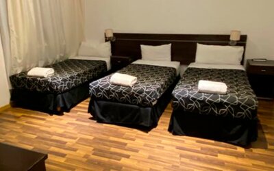 Guest room with three single beds, black patterned bedding, white towels, bedside lights and wooden flooring at Bagu Buenos Aires.