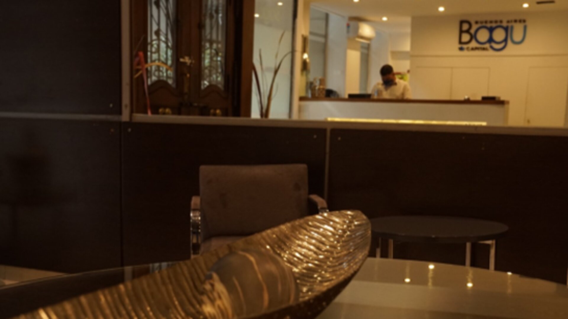 Reception lounge with dark partition, upholstered chairs, decorative bowl and reception desk in the background at Bagu Buenos Aires.