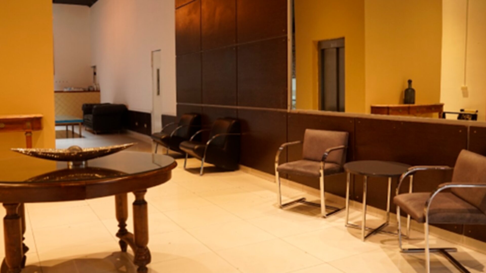 Lobby seating area with upholstered chairs, round tables, decorative bowl and warm yellow walls at Bagu Buenos Aires.
