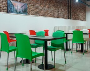 Dining area with red and green chairs, black tables, exposed brick walls and glossy tiled flooring at Bagu Buenos Aires.