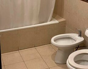 Bathroom with bathtub and shower curtain, toilet, bidet and beige tiled walls and flooring at Bagu Buenos Aires.