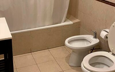 Bathroom with bathtub and shower curtain, toilet, bidet and beige tiled walls and flooring at Bagu Buenos Aires.