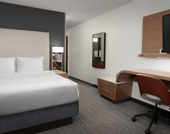 Guest room with a white bed, upholstered headboard, wooden desk, office chair, wall-mounted television and gray carpeting at Courtyard By Marriott Dothan.