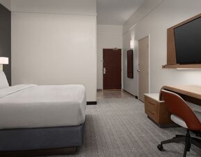 Guest room with white bed, wall-mounted television, wooden desk, office chair and gray carpeting at Courtyard By Marriott Dothan.