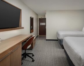 Guest room with two white beds, wooden desk, rust-colored office chair, television and gray patterned carpet at Courtyard By Marriott Dothan.
