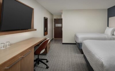 Guest room with two white beds, wooden desk, rust-colored office chair, television and gray patterned carpet at Courtyard By Marriott Dothan.