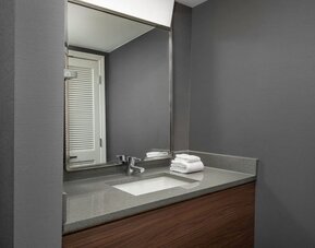 Bathroom vanity with gray countertop, inset sink, large mirror, wooden cabinetry and neatly folded white towels at Courtyard By Marriott Dothan.