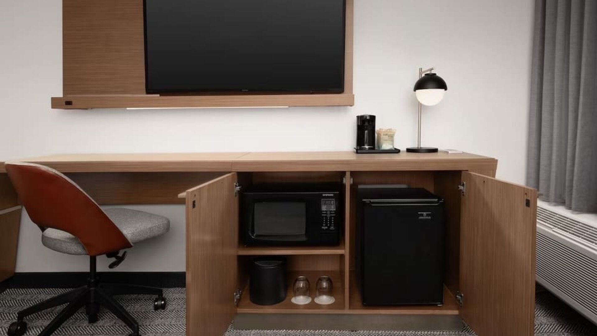 Guest room work area with wall-mounted television, wooden desk, office chair, microwave and mini refrigerator at Courtyard By Marriott Dothan.