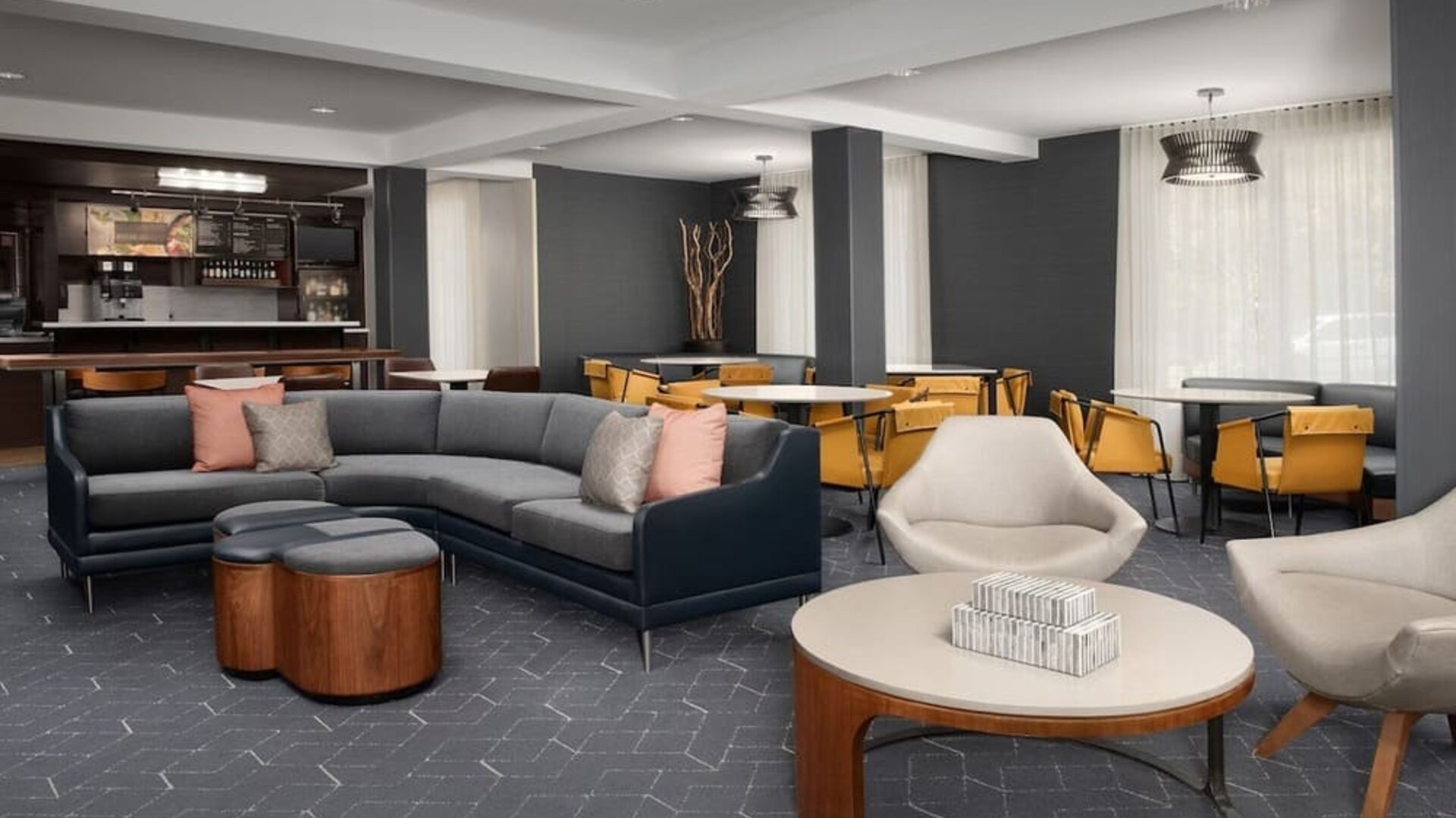 Lobby lounge with gray sectional sofa, upholstered armchairs, round wooden coffee tables and a nearby refreshment counter at Courtyard By Marriott Dothan.
