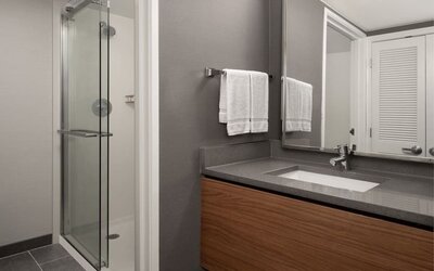Bathroom with glass shower enclosure, wall-mounted showerhead, gray vanity countertop, inset sink and folded white towels at Courtyard By Marriott Dothan.