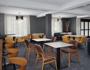 Hotel lounge and dining area with tables, mustard-yellow chairs, brown armchairs, dark walls and large curtained windows at Courtyard By Marriott Dothan.