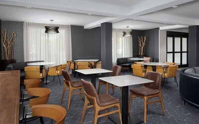 Hotel lounge and dining area with tables, mustard-yellow chairs, brown armchairs, dark walls and large curtained windows at Courtyard By Marriott Dothan.