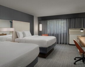 Guest room with two white beds, mirrored headboard panels, wooden desk, office chair, television and curtained window at Courtyard By Marriott Dothan.
