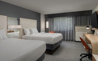 Guest room with two white beds, mirrored headboard panels, wooden desk, office chair, television and curtained window at Courtyard By Marriott Dothan.