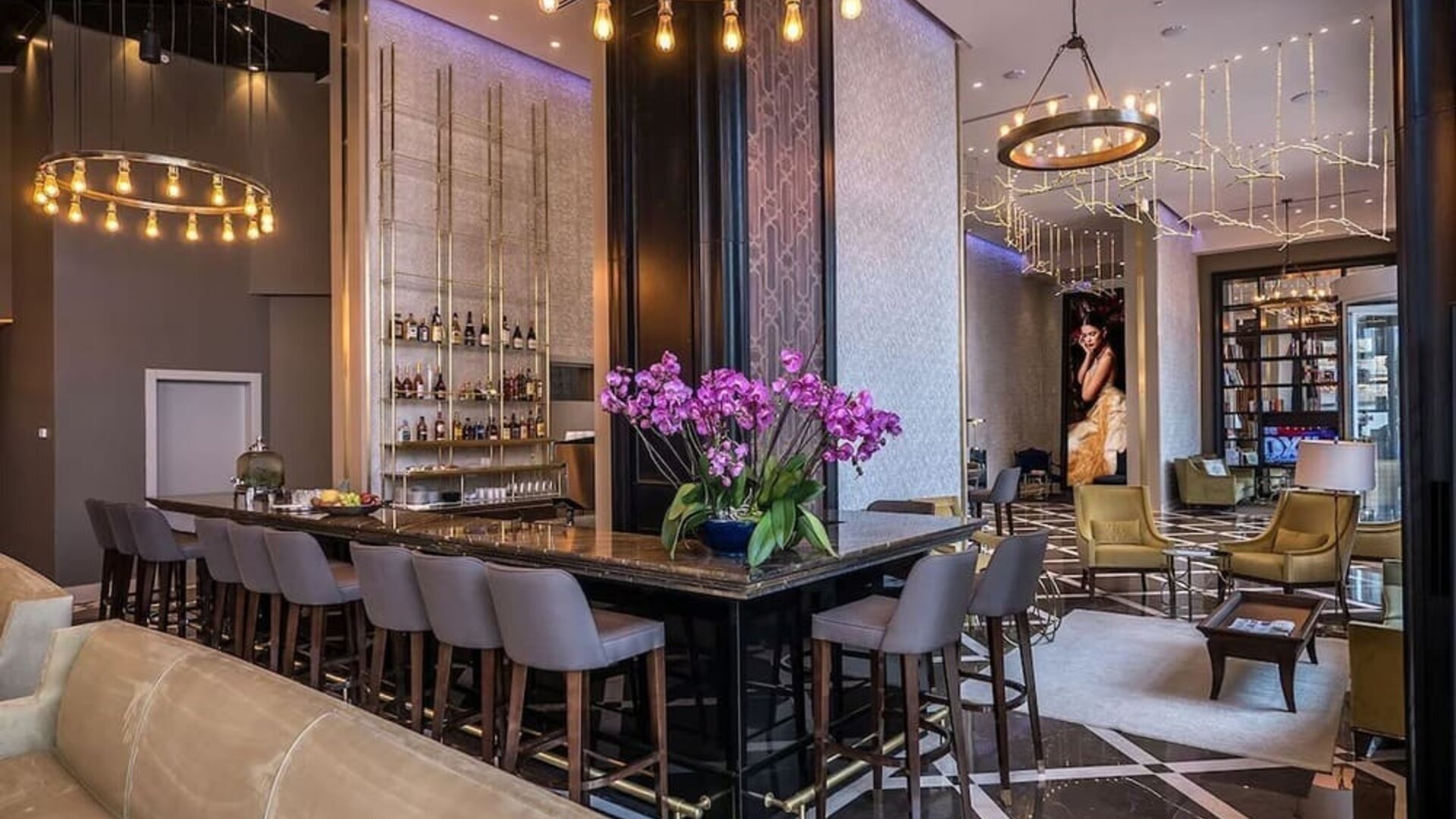 Hotel bar and lounge with a long counter, upholstered stools, purple orchids and gold pendant lighting at David Tower Hotel Netanya.