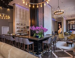 Hotel bar and lounge with a long counter, upholstered stools, purple orchids and gold pendant lighting at David Tower Hotel Netanya.