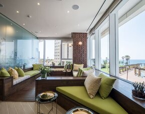Window-side lounge with built-in green seating, patterned cushions and panoramic views of the sea at David Tower Hotel Netanya.