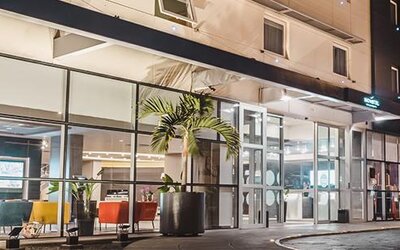 Hotel entrance at night with glass frontage, illuminated signage, palm planters and colourful lounge seating visible inside at Novotel Lima San Isidro.