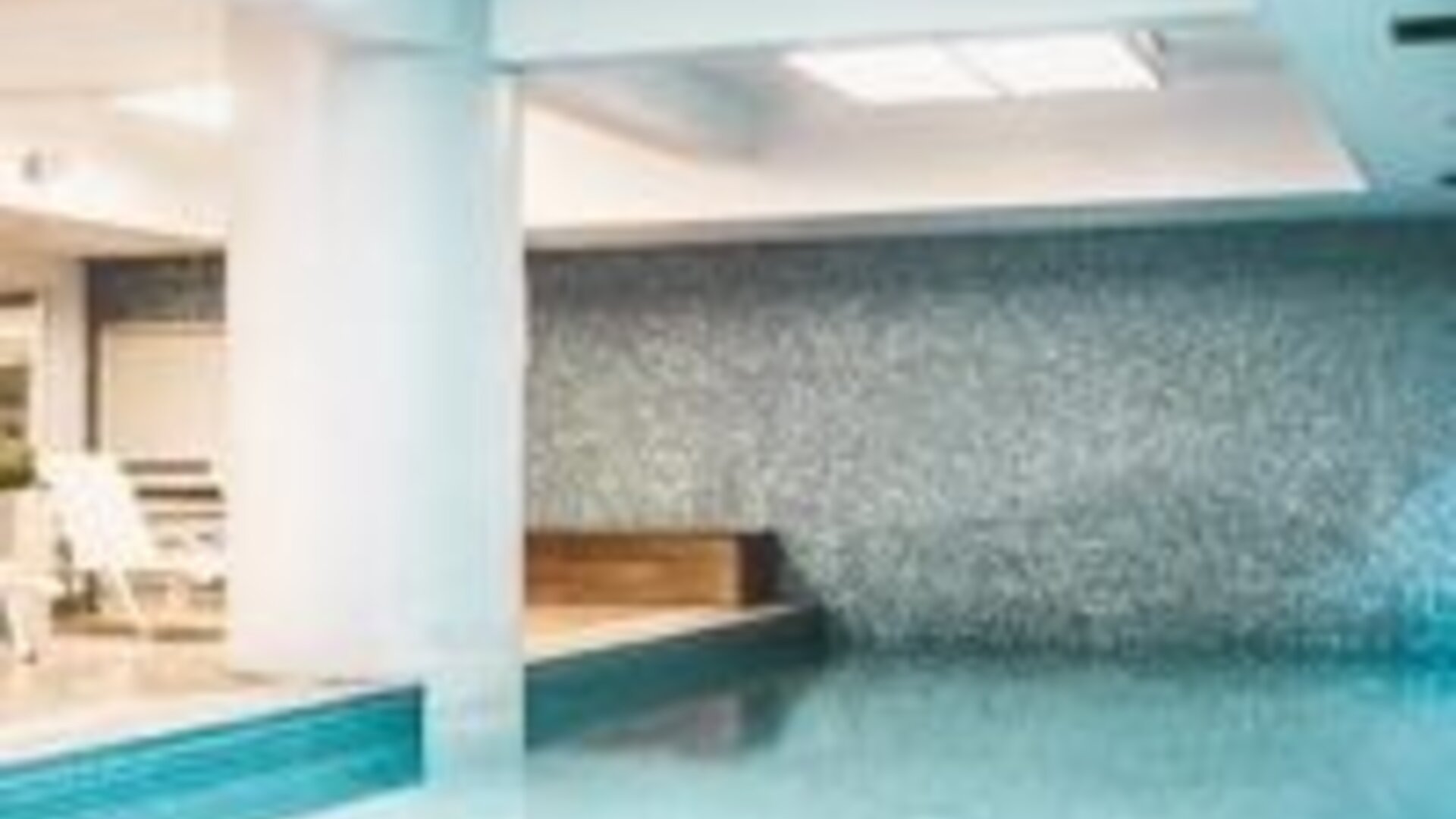 Indoor swimming pool with turquoise water, mosaic-tiled walls, white columns and a built-in poolside bench at Novotel Lima San Isidro.