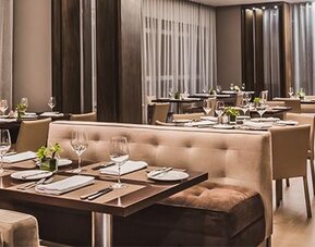 Hotel dining room with neatly arranged tables, upholstered seating, floor-to-ceiling windows and soft lighting at Novotel Lima San Isidro.